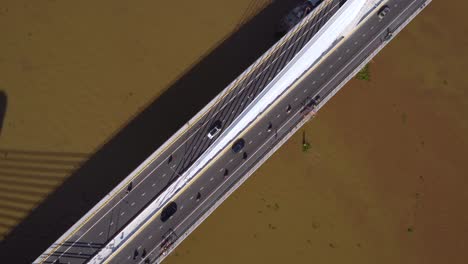 overhead aerial view of traffic on a bridge crossing over muddy looking river