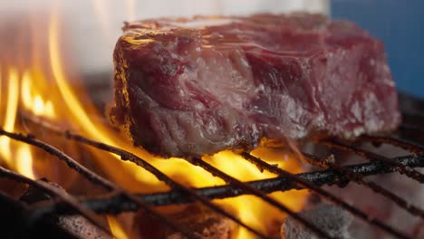 a cook turns a grilled steak amid flames, smoke and barbecue coals