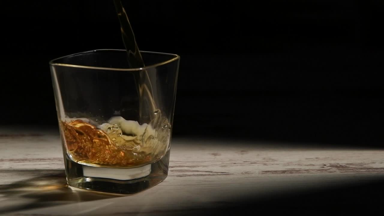 검은 배경에 대한 광선에서 나무 테이블에 버번으로 투명한 유리를 채우는 사람