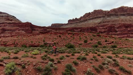 Toma-Aérea-De-Un-Ciclista-De-Montaña-Siguiendo-Un-Sendero-Plano-En-El-Desierto-Rojo-De-Moab