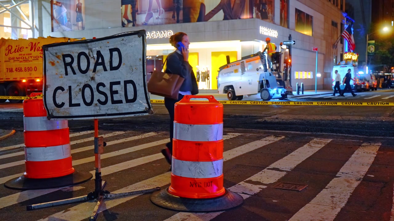 New York, USA, 16 April 2026: Road closed sign and traffic barrels during construction. Close-up of road closed sign and orange traffic barrels on city street with construction background.