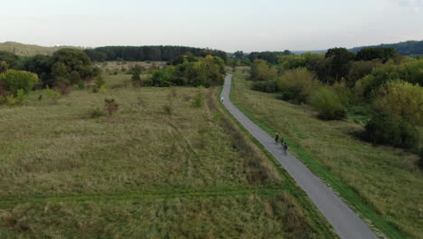 Three-youngsters-ride-bicycle-on-beautiful-flatlands-of-Lithuania,-aerial-following-view