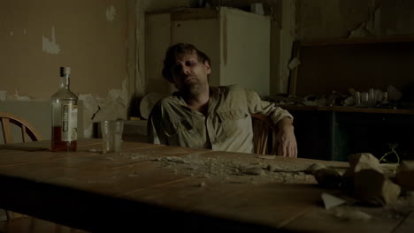 a man passed out on a dirty table with a bottle of alcohol in a dilapidated room