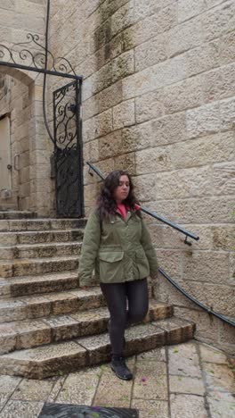 a woman in a green jacket is standing on a stone staircase, in jerusalem