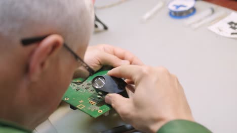 electronic equipment repair shop. the engineer technician solders the printed circuit board of an electronic device under a microscope.