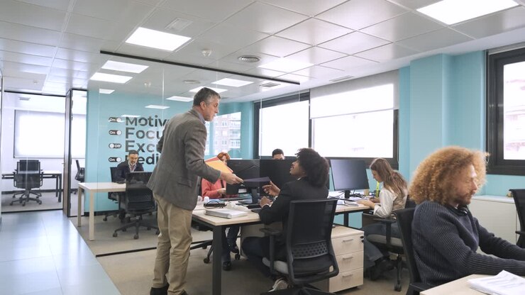 Gerente entregando archivos a empleados en un espacio de coworking.