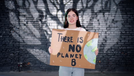 serious young environmental protester holding a cardboard with there is no planet b" inscription and protesting while looking at the camera"