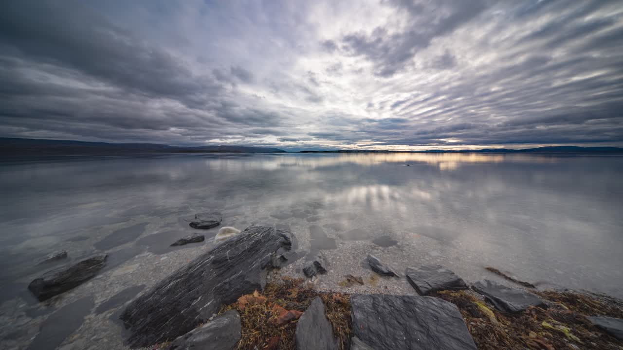 las nubes tormentosas se mueven rápidamente y se reflejan en la superficie espejo del fiordo a medida que la marea se eleva lentamente.