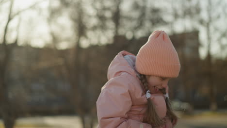 a little girl in a pink cap and jacket sits joyfully on her dad's neck, half of his head snugly tucked in her jacket