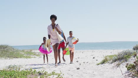 happy african american family with beach equipment walking on beach in a sunny day