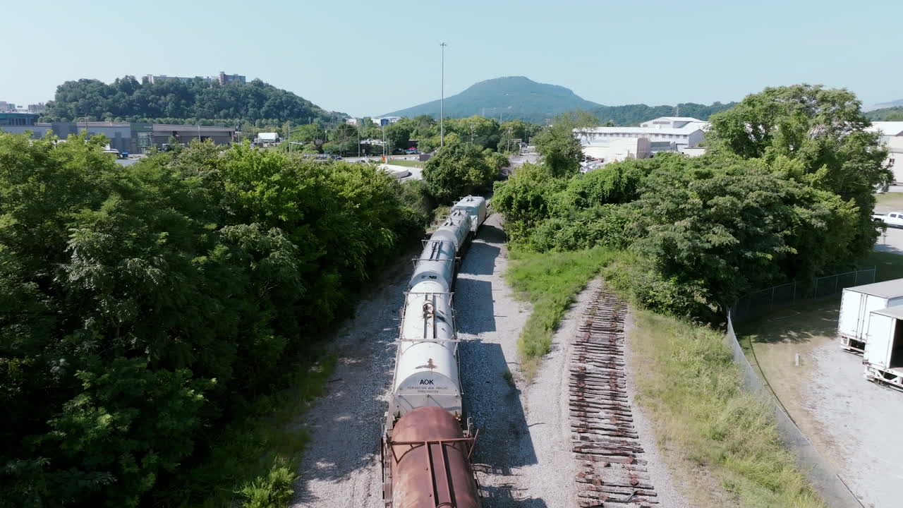 Aerial view of a freight train curving along the tracks near green hills and industrial areas in Chattanooga, Tennessee