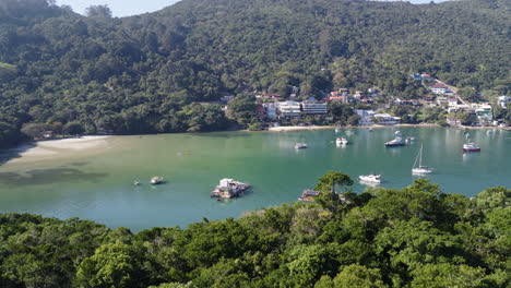 Aerial view of a tropical bay with yachts, forested hills, and clear green waters