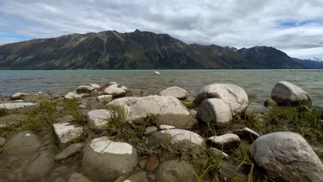 rocas en la orilla del lago tekapo, nueva zelanda con una montaña escarpada en el fondo