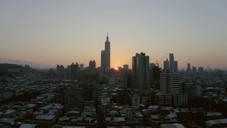 a drone shot of taipei at sunset, on a clear day, with the sun nearly disappearing and taipei 101 in the middle, landmark of taiwan