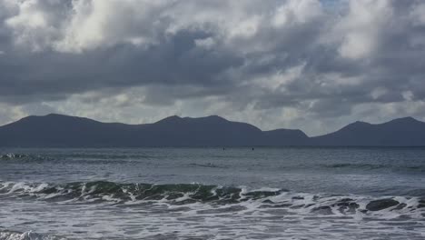 Rough-stormy-shimmering-waves-breaking-under-misty-Snowdonia-mountain-range-with-sunrays-shining-through-overcast-clouds