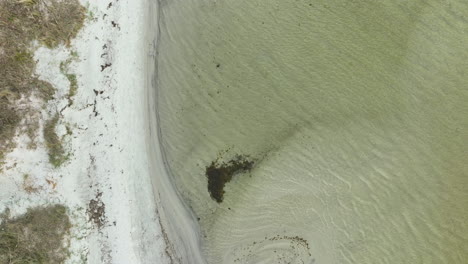 aerial-top-down-view-of-a-sandy-beach-meeting-the-sea,-distinctive-wave-patterns-visible-in-the-water