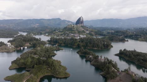 Drone shot circling El Peñón de Guatapé (La Piedra Rock) with lakes and mountains on a cloudy day