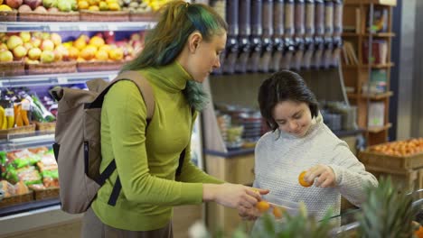 Down-syndrome-girl-with-her-mother-taking-fresh-fruits-from-shelf-in-supermarket