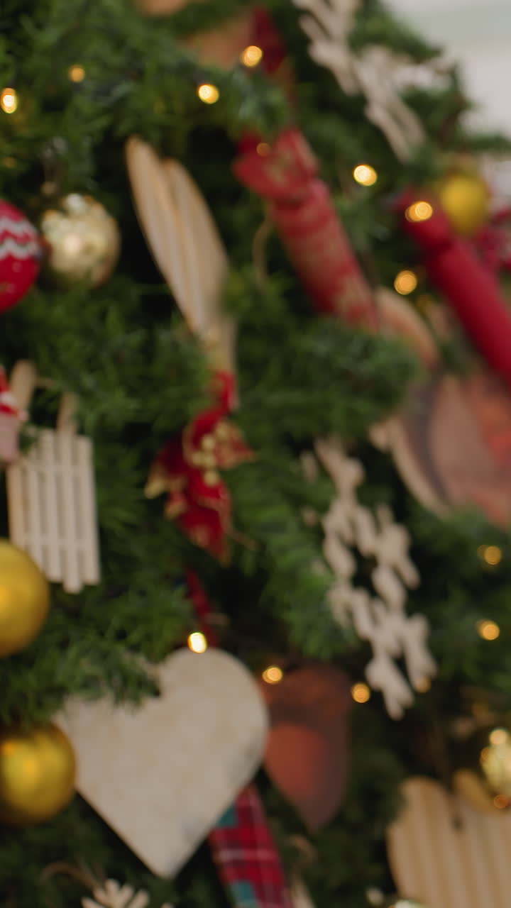 Young woman standing in front of Christmas tree, looking excited and amazed with bokeh light effect in background, shoppers walking by and building inscription visible in vibrant mall