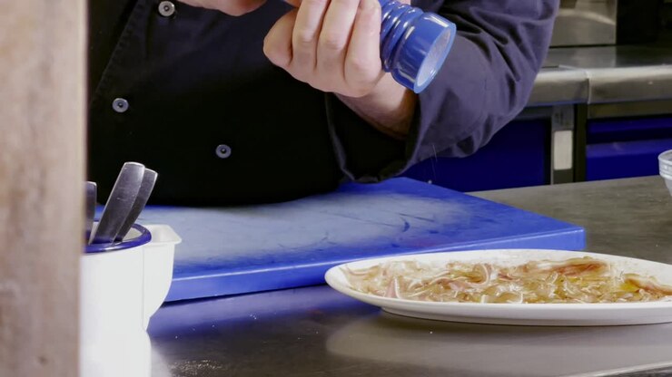 Pepiera che sparge pepe su carpaccio di orecchie di maiale