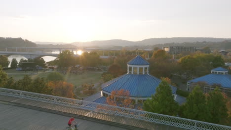 aerial flyover the walnut street bridge while people and bikers go across with coolidge park and the carousel in the background during sunset