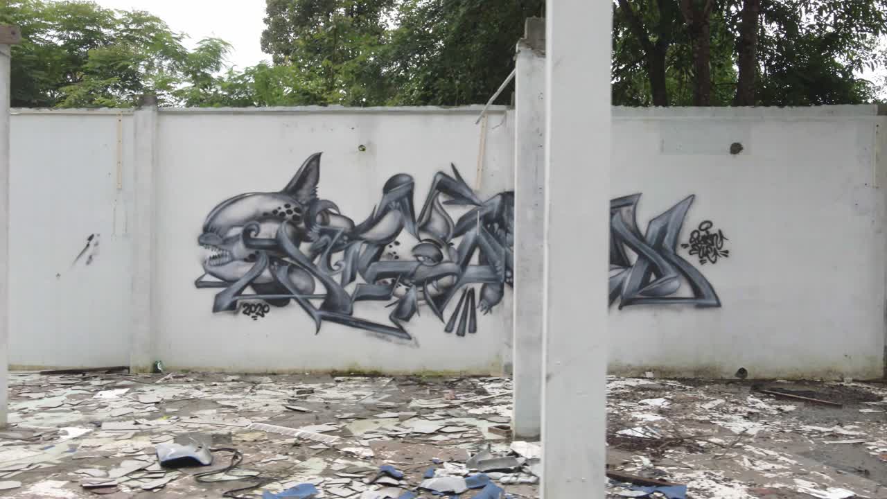 movimento lento a destra, colpo di autocarro laterale di un edificio in rovina con graffiti e materiali da costruzione rotti con la giungla dietro