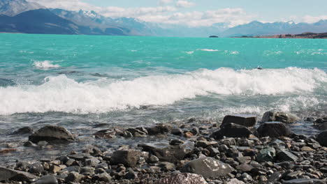 aqua blue waves from glacial melt crash on rocky shoreline in new zealand