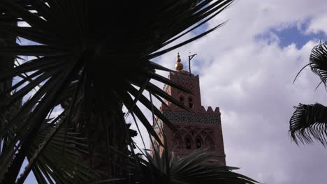 a steady shot of an ancient minaret framed by lush palm leaves – an iconic view of marrakesh's historic beauty of a famous mosque in the medina