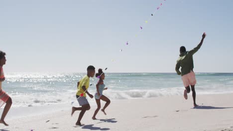 familia afroamericana sonriente corriendo y volando cometa en una playa soleada