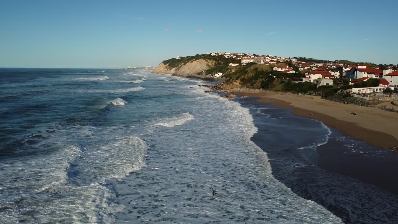 Coastal scene with beach, waves, and houses on a cliff