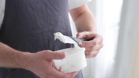 the artist stands and stirs the white paint in the vessel with a spatula the artist stands and stirs the white paint in the vessel with a spatula creative workshop in white tones the process of creating a picture brush movement