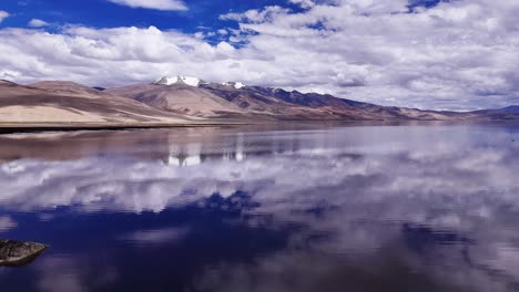 deep blue brackish high altitude lake drone low fly over with mirror flat reflection of snow caped himalayan mountains