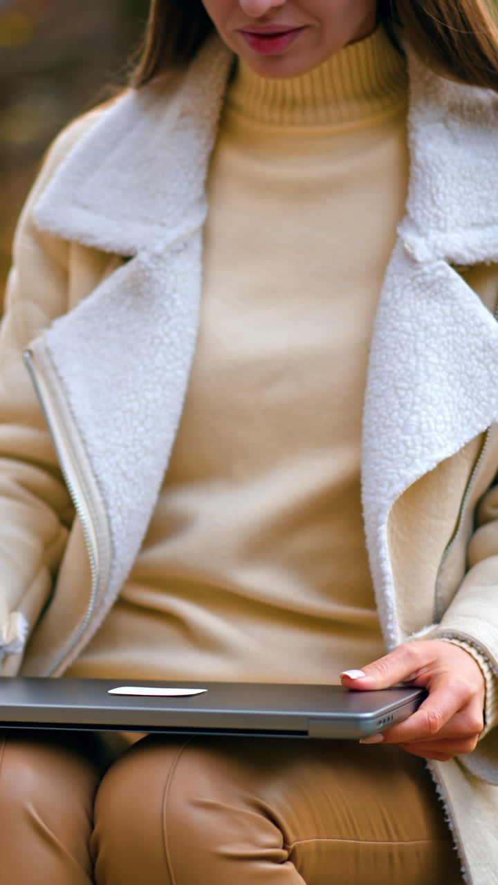 Attractive woman sitting outdoors on the wooden table opens her laptop. Freelancing lady starting work in the nature in autumn park. Vertical video