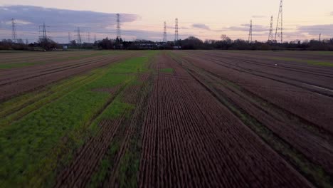 Aerial-shot-of-flooded-field-rising-to-electrical-pylons-during-sunset-UK