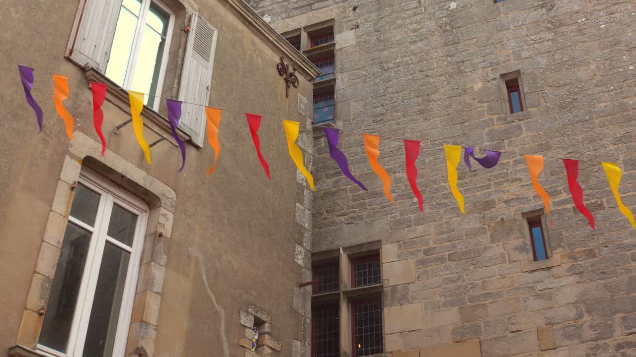 Colorful festive bunting strung across buildings over street in Guérande, France.