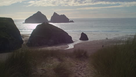 view from sand dunes of shimmering sunlight on beach and rocks in holywell bay at sunset, cornwall, england - wide shot