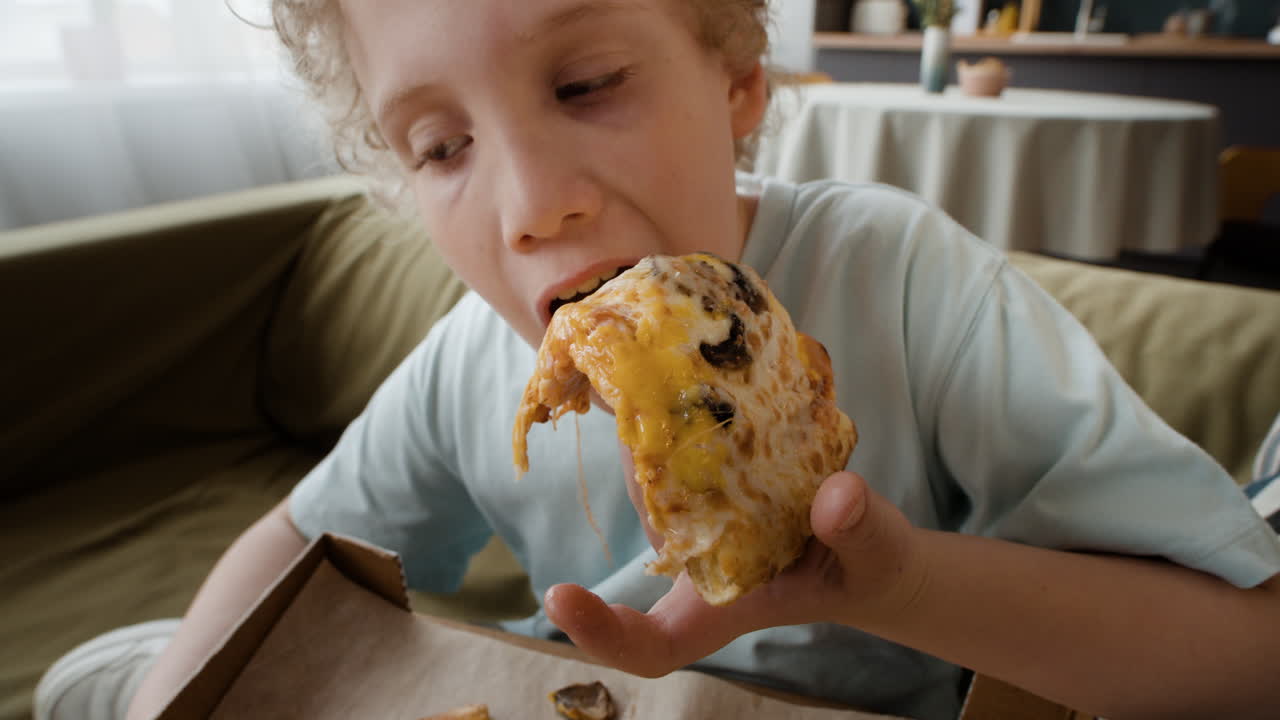 Young Boy Enjoying a Cheesy Pizza Slice at Home