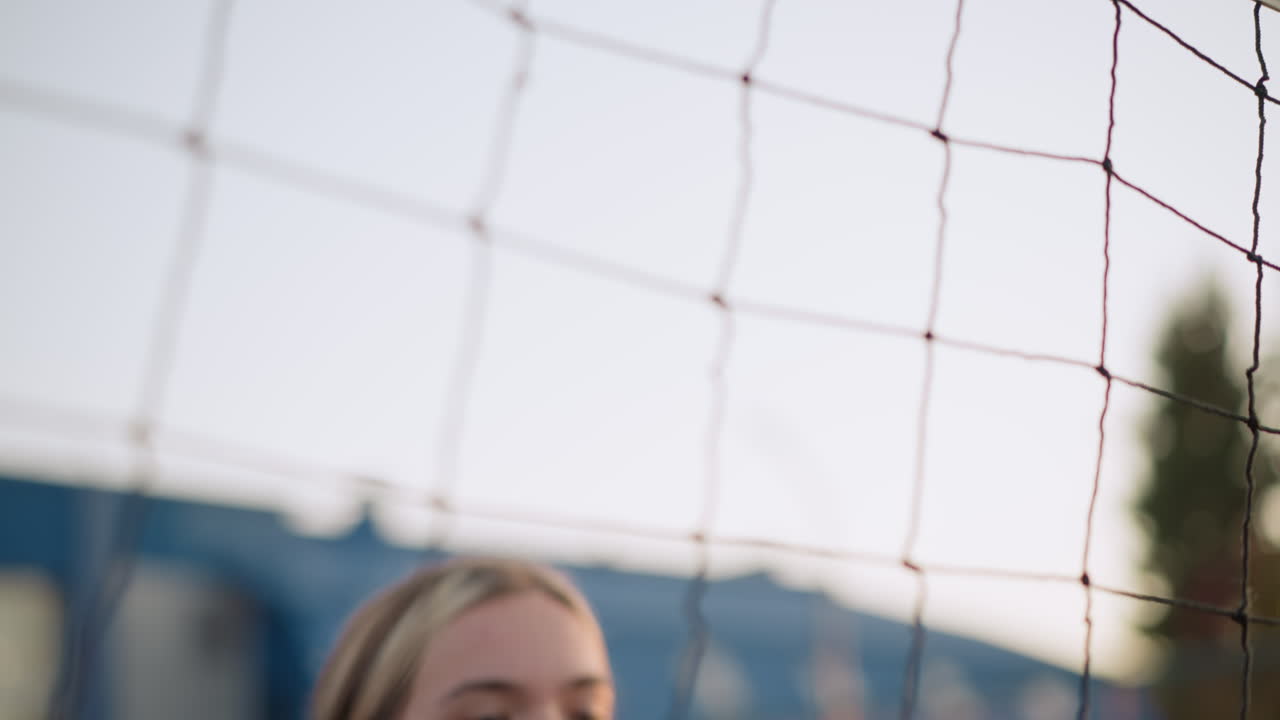 여자 선수가 볼을 치고 점프하는 장면, 망 위에서 공을 때리기 위해 손을 는 장면, 배경에는 건물과 나무가 흐릿하게 보이는 장면, 손과 팔이 초점을 맞추고 있다.