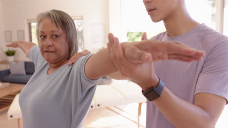 Physiotherapist assisting senior woman with arm stretching exercise in clinic