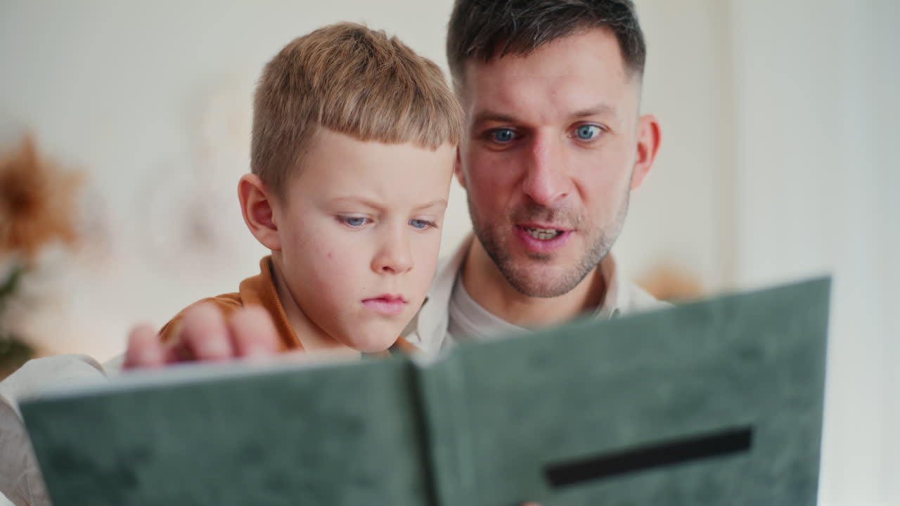 아버지 와 어린 소년 은 가족 앨범 에 있는 사진 을 관심 으로 바라본다