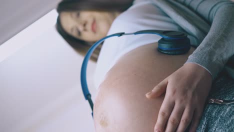 mujer embarazada con auriculares en bailes del vientre a la luz de la lámpara