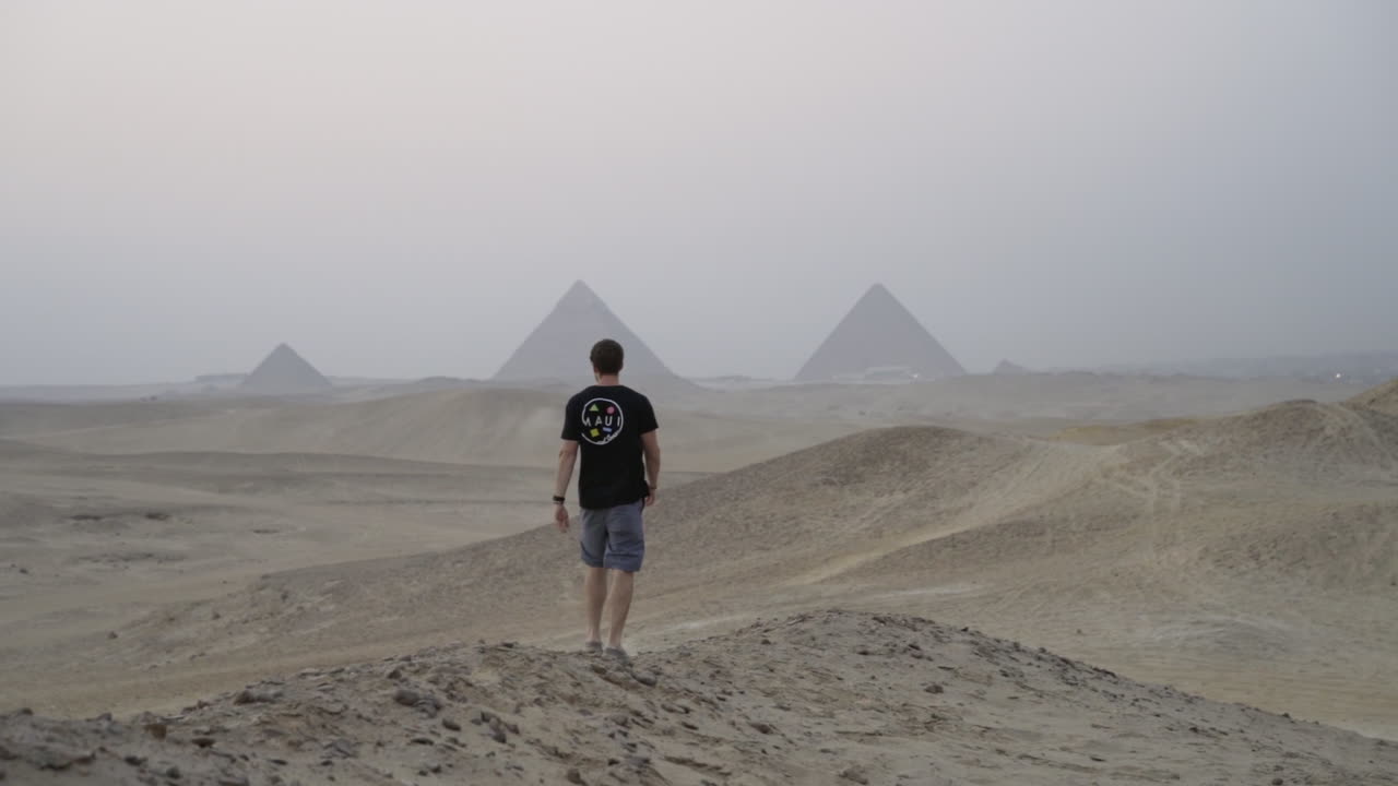 Man walks away towards Great Pyramids of Giza in distance at sunset