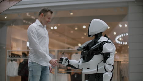 a man in a shirt communicates with a white robot asking questions and pressing the screen with his fingers