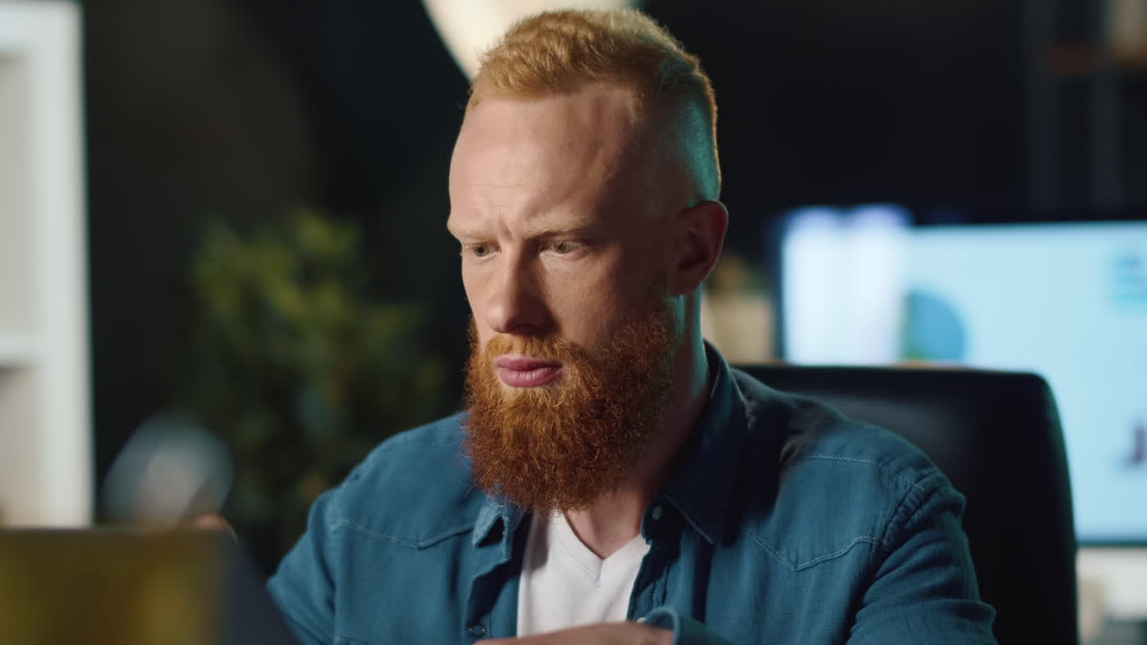 hombre hipster enfocado leyendo mensajes en una computadora portátil en la oficina nocturna.