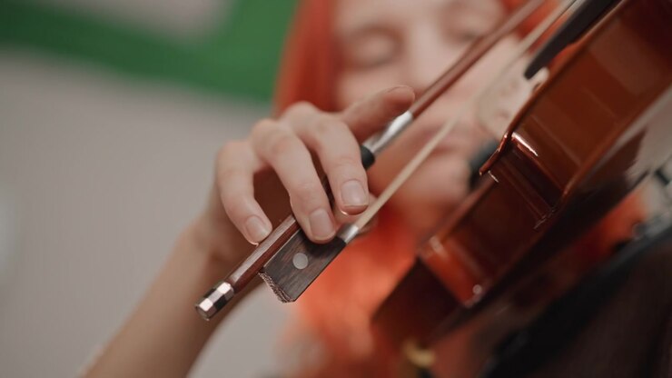 Primo piano di archetto di violino, musicista dai capelli rossi, scene di archetto espressive catturano il contatto dinamico tra crine di cavallo e corde, luce soffusa dell'aula, performance concentrata e controllo tonale.