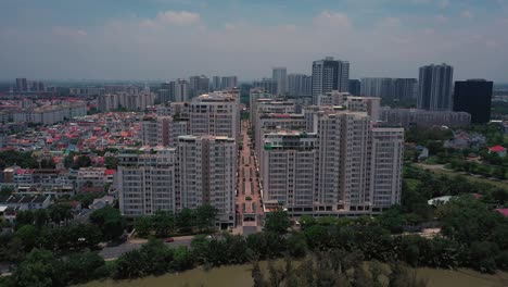 Dramatic-drone-Fly-in-to-central-road-between-tall-buildings-of-a-massive-symmetrical-housing-estate-on-sunny-day-featuring-river-frontage,-towers,-rooftops-and-gardens