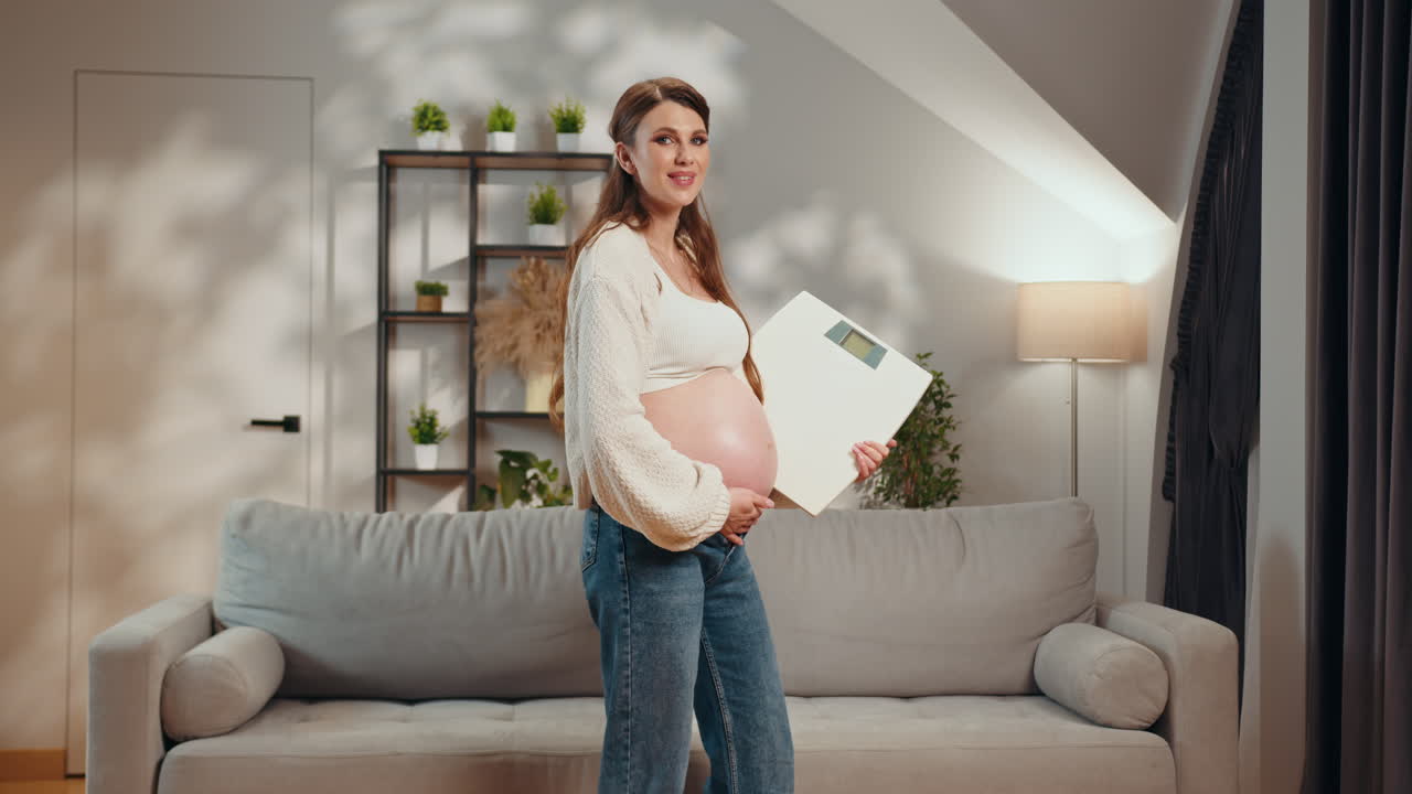 Pregnant woman holding scale in living room monitoring weight gain during pregnancy feeling happy