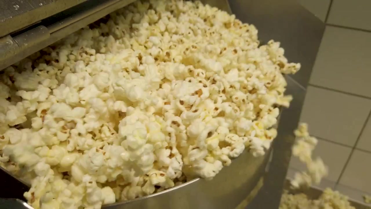 Ripresa in tilt di una cascata di popcorn che fuoriesce dalla macchina per popcorn industriale.