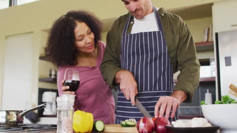 happy diverse couple preparing food together in kitchen, man chopping vegetables embraced by partner