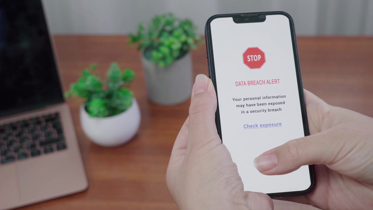 Un avviso AI di violazione dati con simbolo di stop appare su un telefono mentre un pollice si avvicina al link "Verifica esposizione" su una scrivania ordinata.